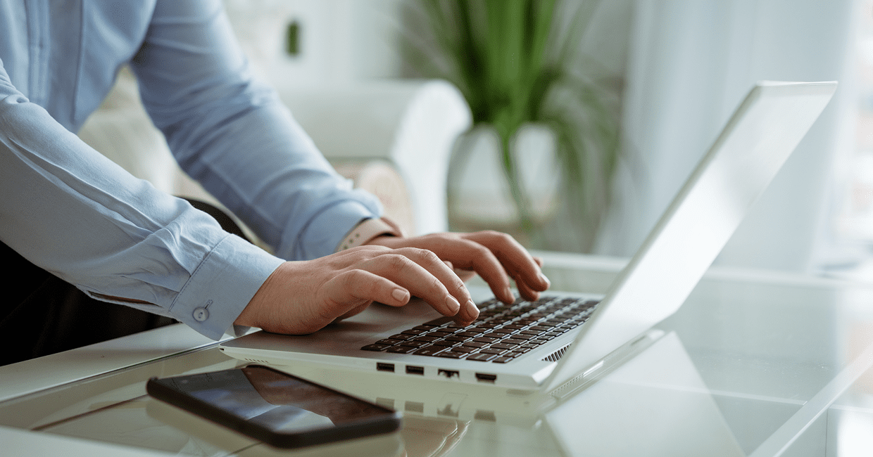 Person typing on a laptop near smartphone.