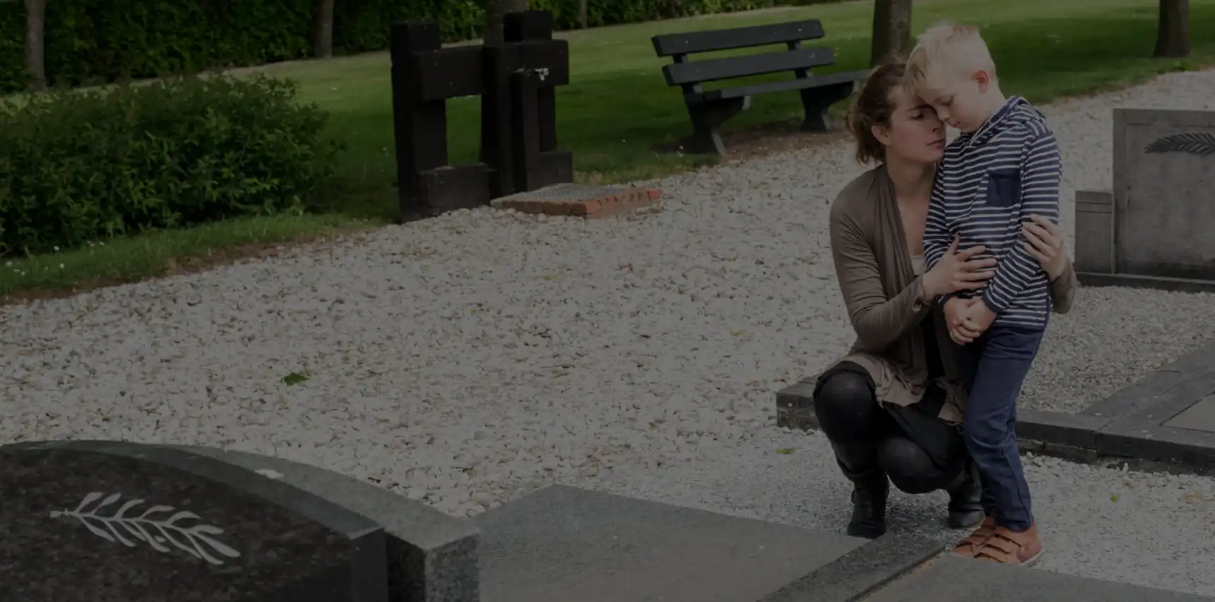 A woman sitting on a stone bench in a park with green grass and benches in the background.