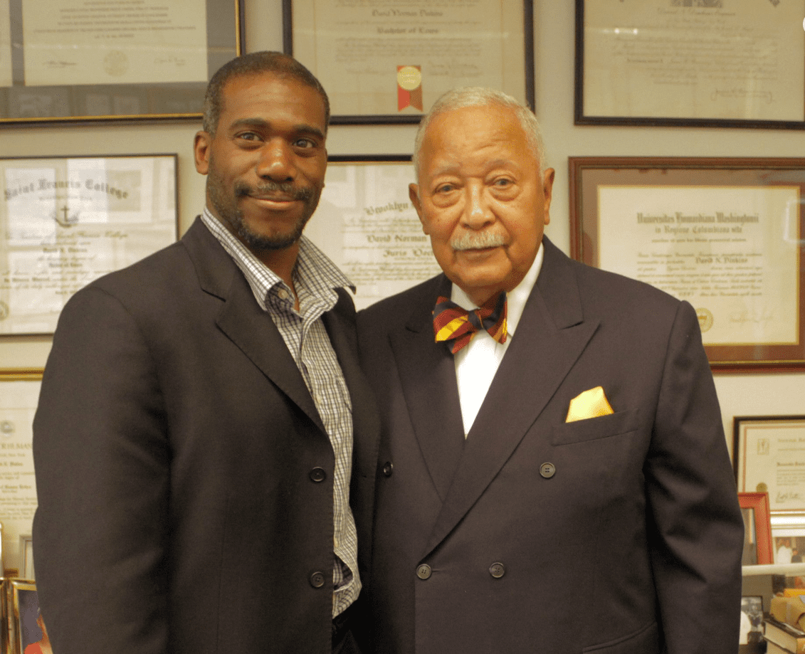Two men posing together in formal attire in an office setting.