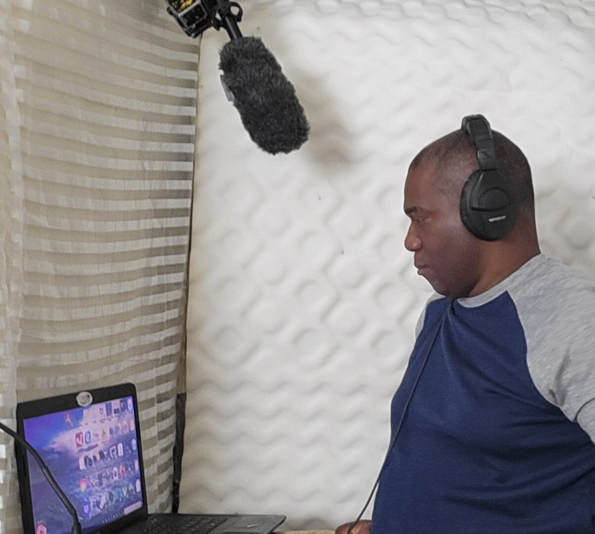 Man recording audio with headphones and microphone in a soundproof booth.